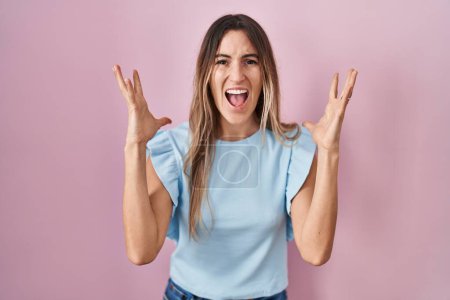 Foto de Mujer hispana joven de pie sobre fondo rosa celebrando loco y loco por el éxito con los brazos levantados y los ojos cerrados gritando emocionado. concepto ganador - Imagen libre de derechos