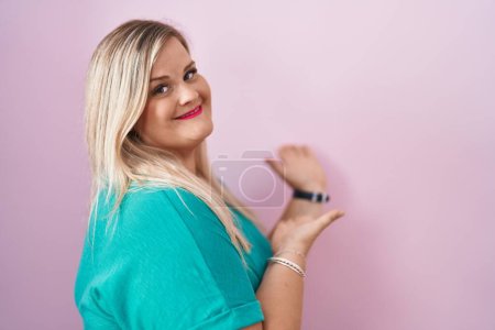 Téléchargez les photos : Blanc plus taille femme debout sur fond rose invitant à entrer souriant naturel avec la main ouverte - en image libre de droit