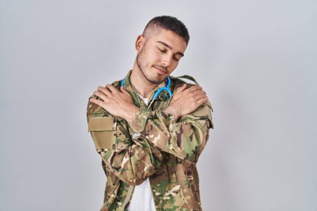 Photo for Young hispanic doctor wearing camouflage army uniform hugging oneself happy and positive, smiling confident. self love and self care - Royalty Free Image