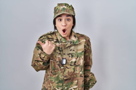 Téléchargez les photos : Jeune femme sud-asiatique portant uniforme camouflage armée surpris pointant avec le doigt de la main sur le côté, bouche ouverte expression étonnée. - en image libre de droit