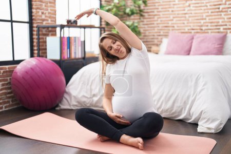 Téléchargez les photos : Jeune femme enceinte faisant de l'exercice préparatoire assis sur un tapis de yoga dans la chambre - en image libre de droit