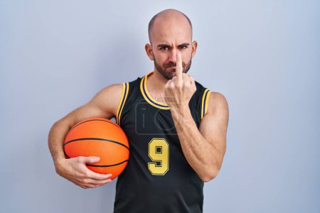 Téléchargez les photos : Young bald man with beard wearing basketball uniform holding ball showing middle finger, impolite and rude fuck off expression - en image libre de droit