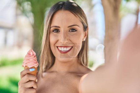 Photo for Young beautiful hispanic woman make selfie by camera eating ice cream at park - Royalty Free Image