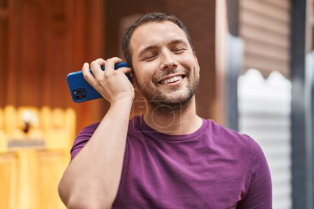 Téléchargez les photos : Young man smiling confident listening audio message by the smartphone at street - en image libre de droit