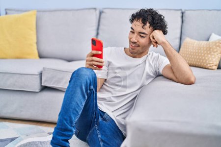 Photo for Young hispanic man using smartphone sitting on floor at home - Royalty Free Image