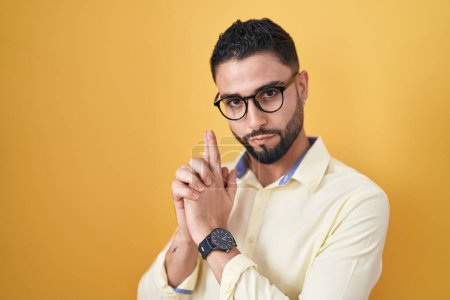 Foto de Hispanic young man wearing business clothes and glasses holding symbolic gun with hand gesture, playing killing shooting weapons, angry face - Imagen libre de derechos
