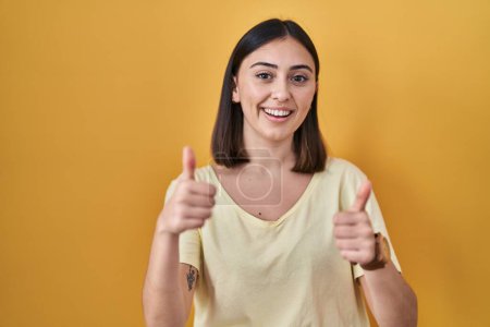 Photo for Hispanic girl wearing casual t shirt over yellow background success sign doing positive gesture with hand, thumbs up smiling and happy. cheerful expression and winner gesture. - Royalty Free Image