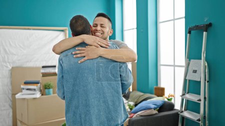Foto de Dos hombres sonriendo confiados abrazándose en un nuevo hogar - Imagen libre de derechos