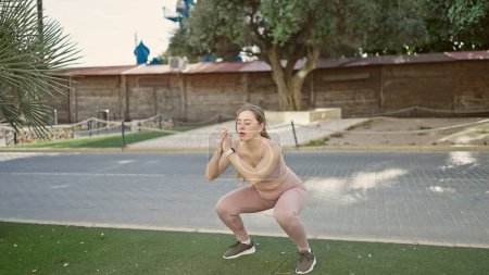Photo for Young blonde woman wearing sportswear doing legs exercise at park - Royalty Free Image