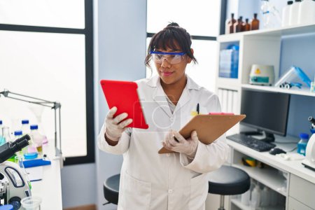 Photo for Young beautiful latin woman scientist using touchpad reading document at laboratory - Royalty Free Image