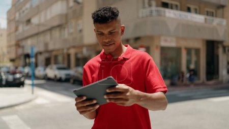 Téléchargez les photos : Jeune homme latin souriant confiant en utilisant touchpad à la rue - en image libre de droit