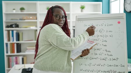 Téléchargez les photos : Femme africaine avec professeur de cheveux tressés donnant des leçons de mathématiques à la bibliothèque universitaire - en image libre de droit
