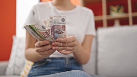 Téléchargez les photos : Jeune femme blonde comptant les billets de banque en roubles russes assis sur le canapé à la maison - en image libre de droit