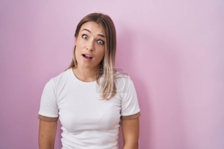 Photo for Blonde caucasian woman standing over pink background in shock face, looking skeptical and sarcastic, surprised with open mouth - Royalty Free Image