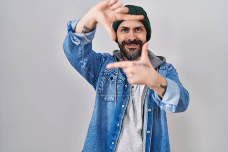 Téléchargez les photos : Young hispanic man with tattoos wearing wool cap smiling making frame with hands and fingers with happy face. creativity and photography concept. - en image libre de droit