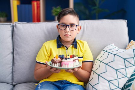 Téléchargez les photos : Jeune enfant hispanique tenant bonbons gâteau détendu avec une expression sérieuse sur le visage. simple et naturel regardant la caméra. - en image libre de droit