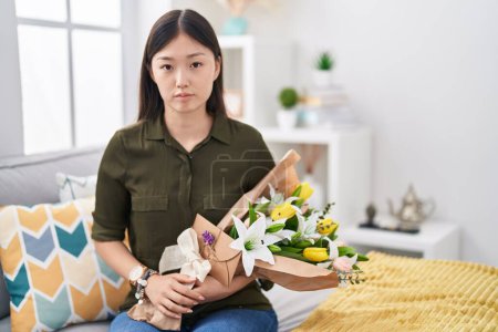 Téléchargez les photos : Jeune femme chinoise tenant un bouquet de fleurs blanches détendues avec une expression sérieuse sur le visage. simple et naturel regardant la caméra. - en image libre de droit