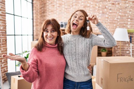 Téléchargez les photos : Mère et fille déménageant dans une nouvelle maison tenant des clés célébrant la réalisation avec un sourire heureux et l'expression gagnante avec la main levée - en image libre de droit