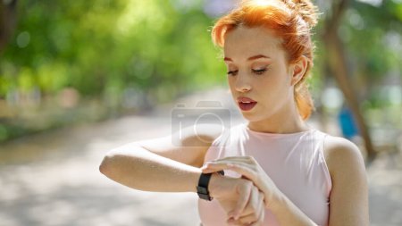 Photo for Young redhead woman wearing sportswear looking watch at park - Royalty Free Image