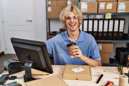 Téléchargez les photos : Jeune homme blond ecommerce travailleur d'affaires boire du café en utilisant l'ordinateur au bureau - en image libre de droit