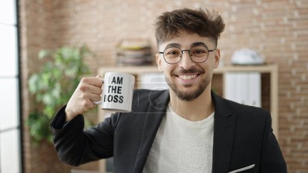 Foto de Trabajador de negocios árabe joven sonriendo confiado bebiendo café en la oficina - Imagen libre de derechos