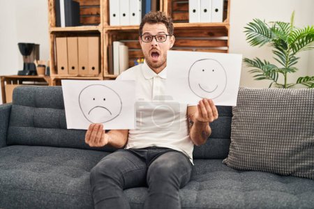 Photo for Young hispanic man working on depression holding sad to happy emotion paper in shock face, looking skeptical and sarcastic, surprised with open mouth - Royalty Free Image