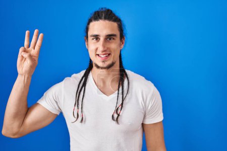Photo for Hispanic man with long hair standing over blue background showing and pointing up with fingers number three while smiling confident and happy. - Royalty Free Image