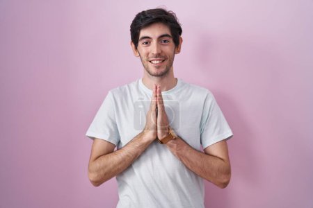 Photo for Young hispanic man standing over pink background praying with hands together asking for forgiveness smiling confident. - Royalty Free Image