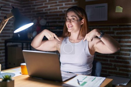 Photo for Brunette woman working at the office at night looking confident with smile on face, pointing oneself with fingers proud and happy. - Royalty Free Image
