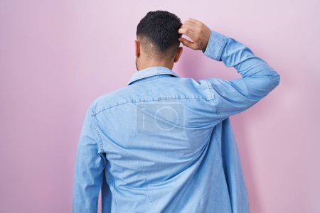 Téléchargez les photos : Hispanic young man standing over pink background backwards thinking about doubt with hand on head - en image libre de droit