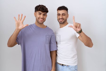 Foto de Homosexual gay pareja de pie sobre blanco fondo mostrando y apuntando hacia arriba con los dedos número siete mientras sonriendo confidente y feliz. - Imagen libre de derechos