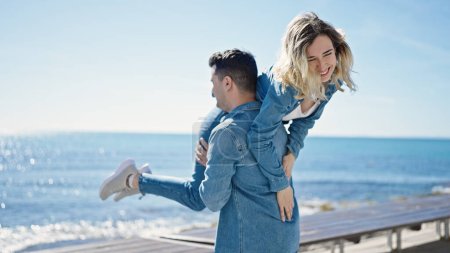 Téléchargez les photos : Homme et femme couple souriant confiant tenant petite amie sur l'air tournant au bord de la mer - en image libre de droit