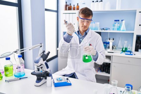Photo for Young man scientist pouring liquid on test tube at laboratory - Royalty Free Image
