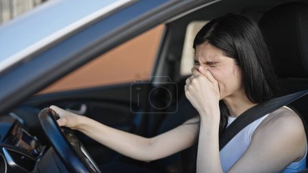 Téléchargez les photos : Jeune belle femme hispanique fatiguée assise sur la voiture bâillant dans la rue - en image libre de droit
