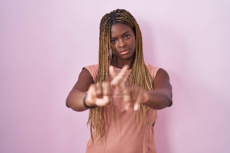 Téléchargez les photos : Femme afro-américaine avec des cheveux tressés debout sur fond rose expression de rejet en croisant les doigts faisant signe négatif - en image libre de droit