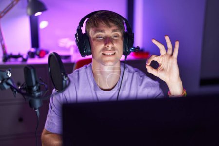 Photo for Caucasian blond man playing video games doing ok sign with fingers, smiling friendly gesturing excellent symbol - Royalty Free Image