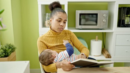 Photo for Mother and son reading book while breastfeeding baby at dinning room - Royalty Free Image