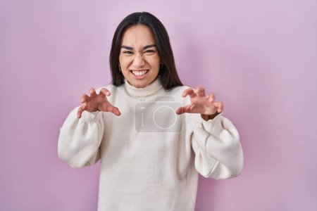 Téléchargez les photos : Jeune femme sud-asiatique debout sur fond rose souriant drôle faisant griffe geste comme chat, expression agressive et sexy - en image libre de droit