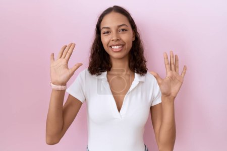 Photo for Young hispanic woman wearing casual white t shirt showing and pointing up with fingers number ten while smiling confident and happy. - Royalty Free Image
