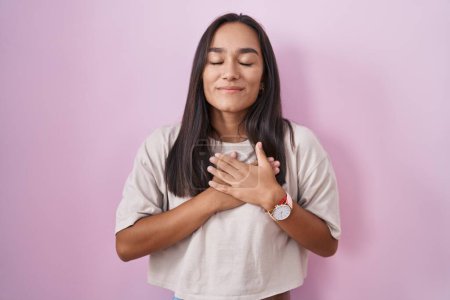 Téléchargez les photos : Jeune femme hispanique debout sur fond rose souriant avec les mains sur la poitrine avec les yeux fermés et geste reconnaissant sur le visage. concept de santé. - en image libre de droit