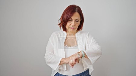 Foto de Mujer de mediana edad mirando reloj con cara seria sobre fondo blanco aislado - Imagen libre de derechos