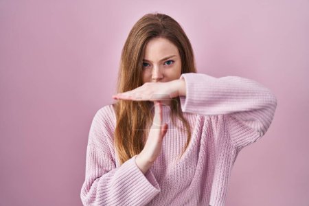 Foto de Joven mujer caucásica de pie sobre fondo rosa haciendo el gesto de tiempo fuera con las manos, rostro frustrado y grave - Imagen libre de derechos