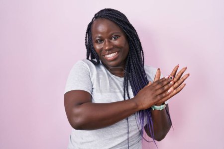 Téléchargez les photos : Jeune femme africaine debout sur fond rose applaudissements et applaudissements heureux et joyeux, souriant mains fiers ensemble - en image libre de droit