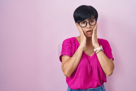 Téléchargez les photos : Jeune femme asiatique aux cheveux courts debout sur fond rose effrayé et choqué, surprise et expression étonnante avec les mains sur le visage - en image libre de droit