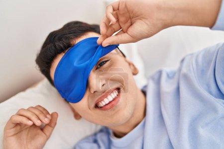 Téléchargez les photos : Jeune homme non binaire portant un masque de sommeil couché sur le lit - en image libre de droit