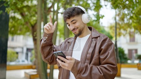 Téléchargez les photos : Jeune homme arabe souriant confiant écoutant de la musique et dansant au parc - en image libre de droit