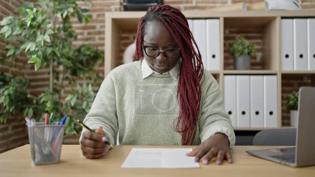 Téléchargez les photos : Femme africaine aux cheveux tressés signant un document au bureau - en image libre de droit