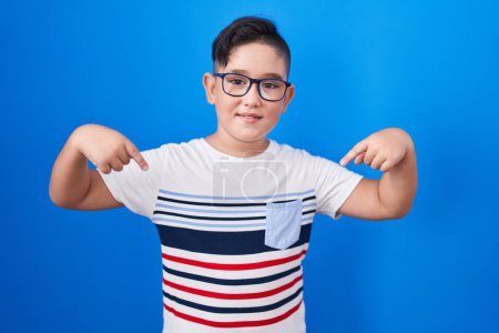 Photo for Young hispanic kid standing over blue background looking confident with smile on face, pointing oneself with fingers proud and happy. - Royalty Free Image