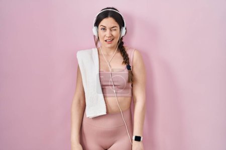 Photo for Young brunette woman wearing sportswear and headphones winking looking at the camera with sexy expression, cheerful and happy face. - Royalty Free Image