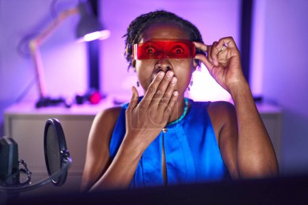 Téléchargez les photos : Femme africaine avec dreadlocks jouer à des jeux vidéo portant des lunettes de réalité virtuelle couvrant la bouche avec la main, choquée et effrayée par l'erreur. expression surprise - en image libre de droit